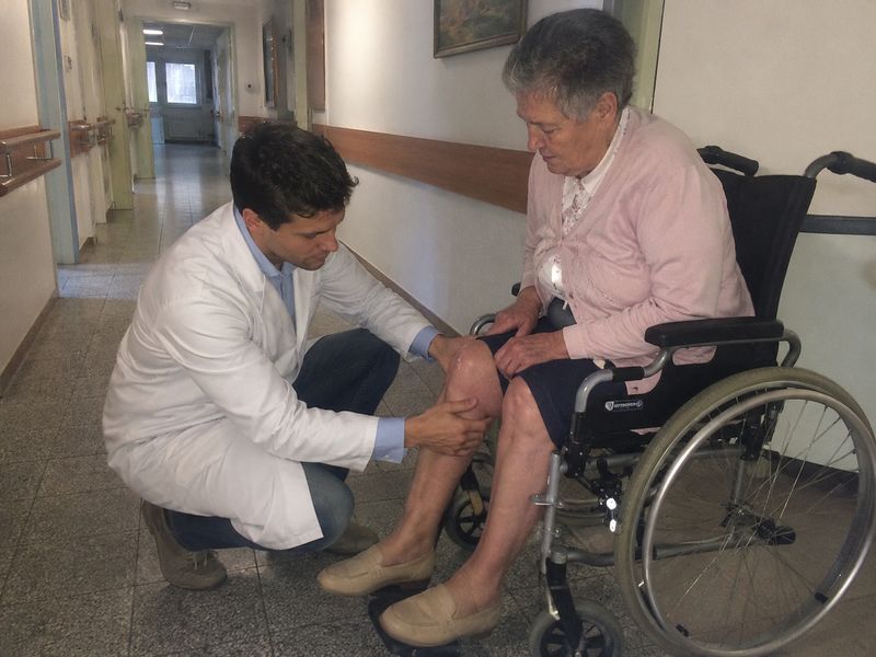 El Dr. Andrés Figueroa examina la rodilla de una paciente en un hogar de ancianos